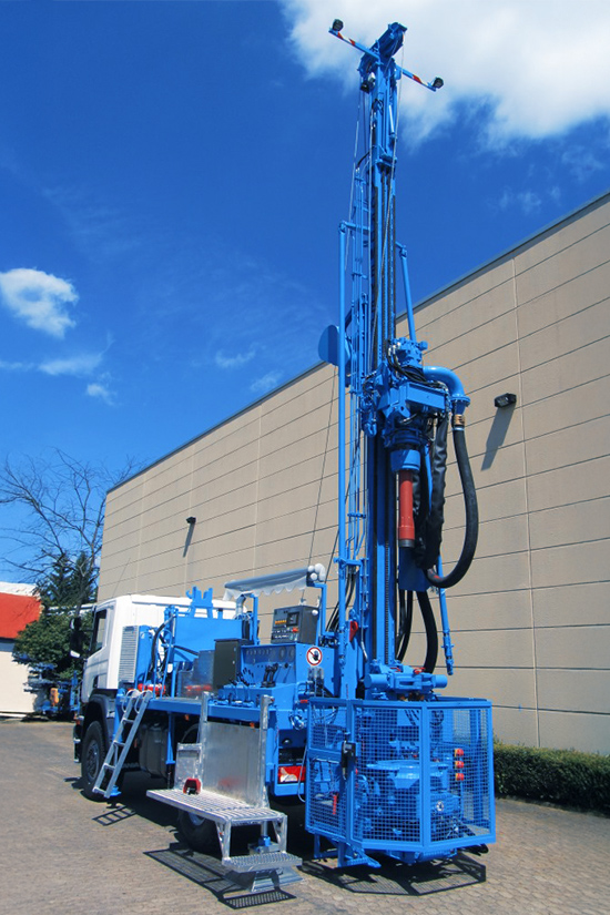 Ein großer blauer Mercedes-Lkw mit Allradreifen aus dem Fuhrpark von Ivers Brunnenbau steht im Freien. Auf der Ladefläche ist eine Bohranlage mit hohem Mast aufgebaut. Im Hintergrund ist ein Gebäude.